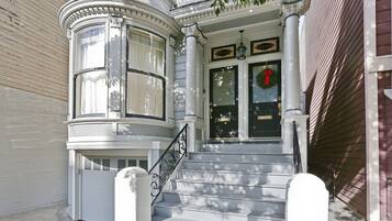 A corner building with a bay window, a set of stairs leading to a door with a wreath, and a number plaque above the door.