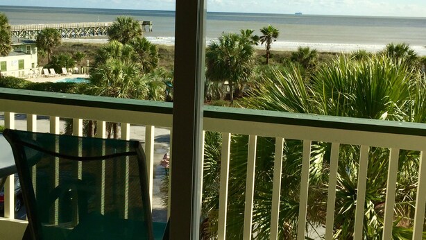 A balcony with a view of the beach, palm trees, and a pier in the distance. - Isle of Palms - 3rd Floor Ocean Front with Private Balcony, Pool, and Pier  (Isle of Palms)