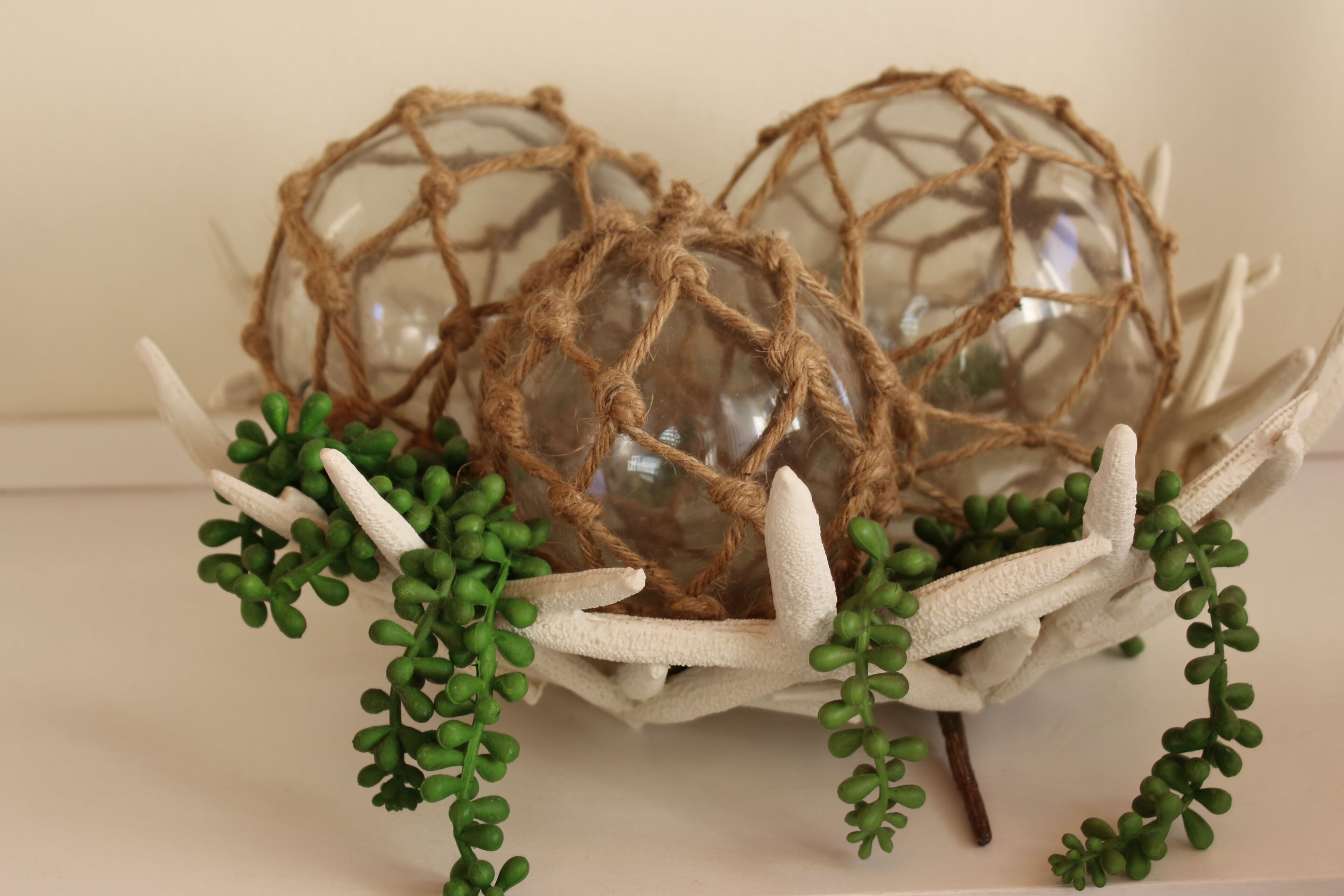A decorative arrangement with glass spheres and a woven structure, surrounded by green foliage.