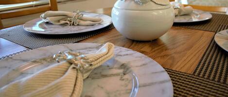 A dining table with a white ceramic bowl and plates with napkins tied with a rope.