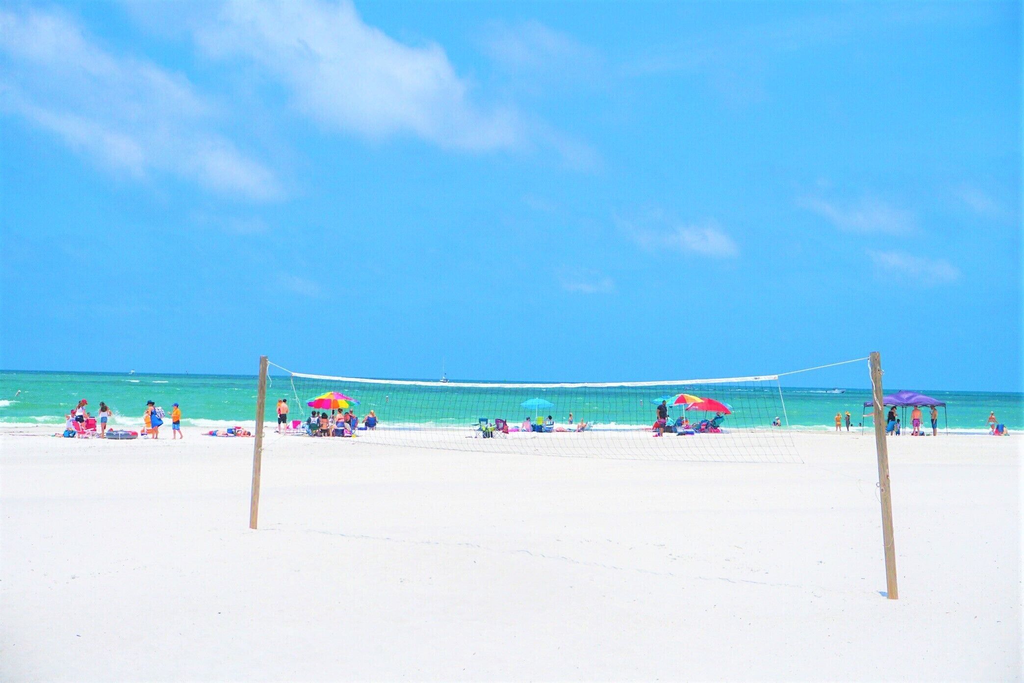 Una cancha de voleibol de playa con red, rodeada de arena blanca y un cielo azul despejado.