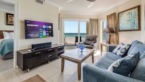A modern living room with a flat-screen TV, a sofa, a coffee table, and a balcony with a view of the sea. - Sunset Vistas Penthouse 601 W Beach Front unit/Treasure Island /St. Pete Beach. (Treasure Island)