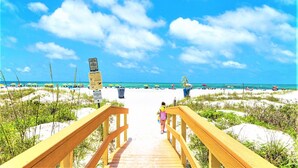 A wooden boardwalk leading to a beach with clear skies and people in the distance. - Sunset Vistas Penthouse 601 W Beach Front unit/Treasure Island /St. Pete Beach. (Treasure Island)