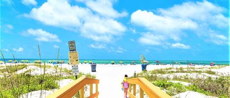 A wooden boardwalk leading to a beach with clear skies and people in the distance.