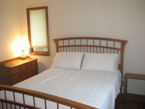 Ein ordentlich bezogenes Bett mit einem Holzkopfende, ein Nachttisch mit Lampe und ein Spiegel an der Wand.