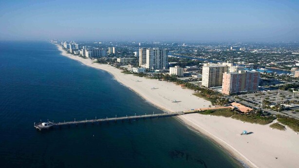 A coastal cityscape with a long beach, high-rise buildings, and a pier extending into the water.