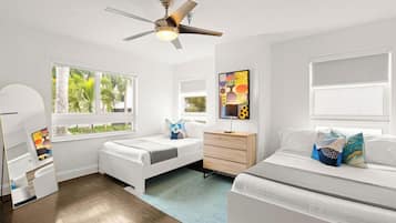 Une chambre moderne avec deux lits, un ventilateur de plafond, une commode et une grande fenêtre donnant sur des palmiers.