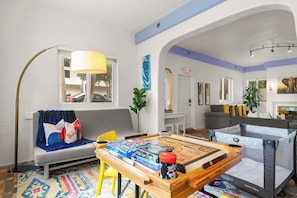 A cozy living room with a sofa, a coffee table with board games, a playpen, and a lamp.