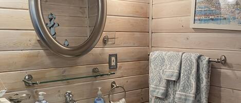 A bathroom with wooden paneling, a white sink, a mirror, a framed picture, and towels.