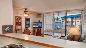 A modern kitchen with a dining area, a TV, and a balcony with a view of the ocean.