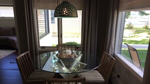 A dining area with a glass table surrounded by striped cushioned chairs, a decorative hanging light fixture, and a view of a backyard through large windows. - FAMILY FRIENDLY COTTAGE SLEEPS 12 !!! BEAUTIFULLY UPDATED (Petoskey)