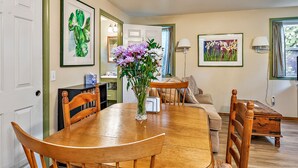 Un coin repas avec une table et des chaises en bois, un vase de fleurs et des œuvres d’art encadrées accrochées aux murs.