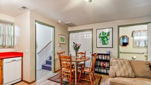 Un salon avec un canapé marron, une table à manger avec des chaises, une bibliothèque et un escalier menant à une autre pièce.