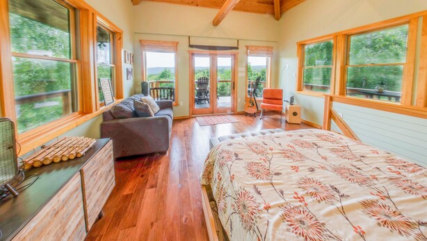 Un dormitorio amplio con una cama grande, vigas de madera en el techo y ventanas amplias que ofrecen vistas al exterior.