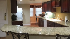 A kitchen with granite countertops, dark wooden cabinets, and a bar area with two stools.