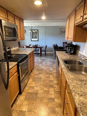 A kitchen with wooden cabinets, a granite countertop, a stainless steel sink, and a dining area with a table and chairs.
