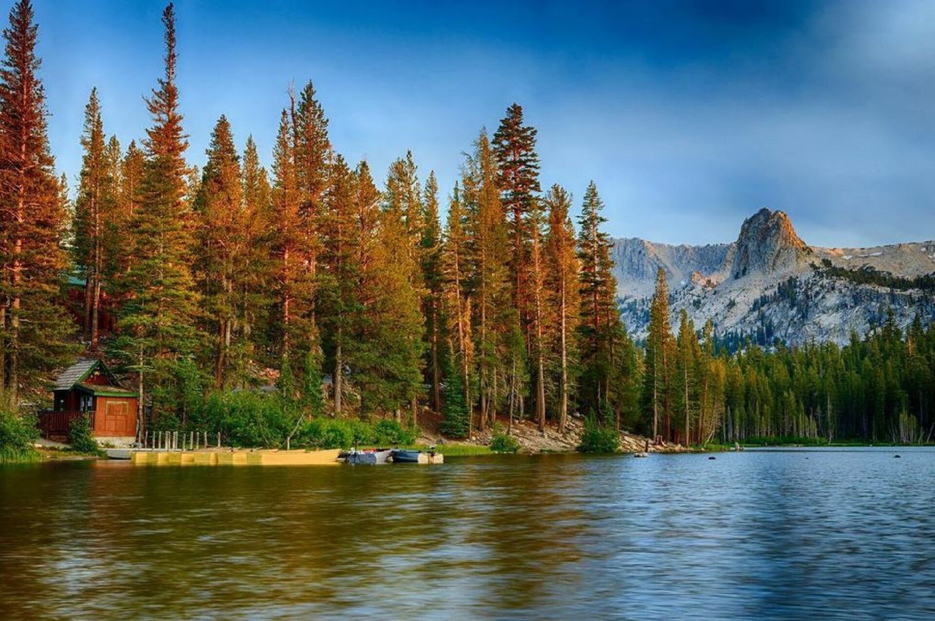 Une cabane au bord d’un lac, avec une montagne en arrière-plan.