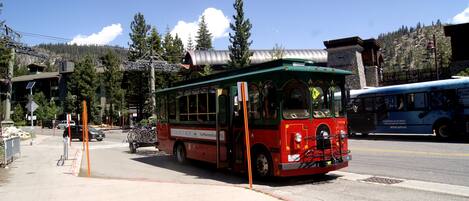 A red and green trolley bus parked at a bus stop with a mountainous backdrop.