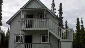 A two-story cabin with a balcony, a staircase, and a small porch. - Kenai River Cabins Front (Soldotna)