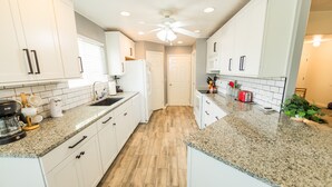 A modern kitchen with white cabinets, granite countertops, and a wooden floor.