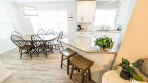 A modern kitchen with white cabinets, a granite countertop, and a dining area with wooden chairs and a table.