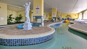 An indoor swimming pool with a central statue, tiled walls, and lounge chairs along the sides.
