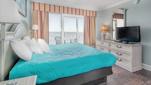 A bedroom with a bed, a television, a dresser, and a window with curtains.