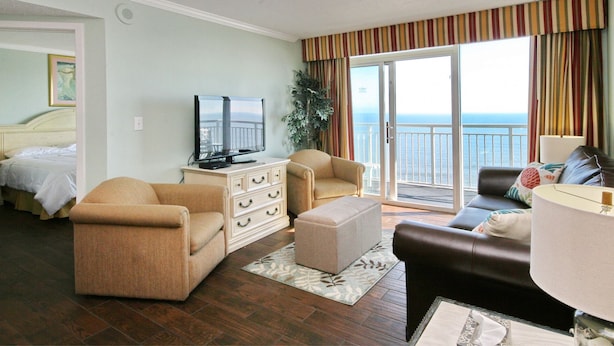 A hotel room with a balcony, a television, a sofa, a chair, and a bed.