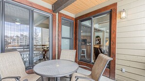 An outdoor patio with a round table and four chairs, large sliding glass doors, and a wooden ceiling. - 2BR Mountain Condo | Walk to Gondola | Pool, Hot Tubs and Balcony! (Steamboat Springs)