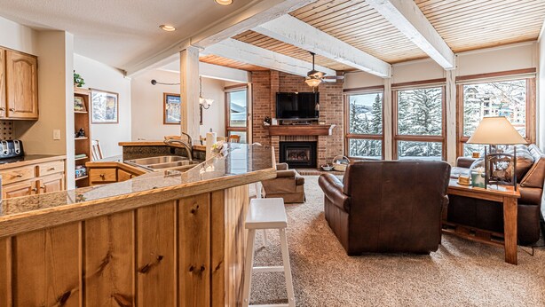 A spacious living area with a fireplace, a bar, and a large window offering a view of the outdoors. - 2BR Mountain Condo | Walk to Gondola | Pool, Hot Tubs and Balcony! (Steamboat Springs)