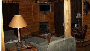 Interior acogedor de una cabaña de troncos, con televisor, lámpara, chimenea y mecedora.