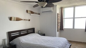A bedroom with a bed, a ceiling fan, an air conditioner, a window with curtains, and a decorative wall piece. - Location,Location,Location "Casa Gelma" WATERFRONT  (Isla Verde)