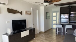 A modern living room with a flat-screen TV, a dining area with bar stools, and a kitchen with a built-in oven. - Location,Location,Location "Casa Gelma" WATERFRONT  (Isla Verde)