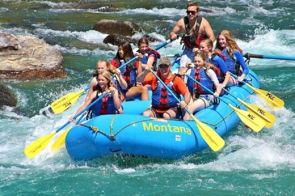 A group of people in a blue inflatable raft with 'Montana' written on it, navigating through a river with rapids.