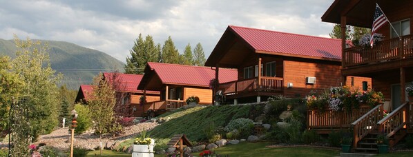 A row of wooden cabins with red roofs, a balcony, and a garden with flowers and shrubs.