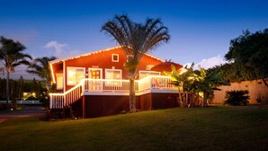 A two-story house with a covered porch, surrounded by a well-maintained lawn and palm trees.