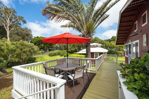 Un espace extérieur abrité, équipé d’une table et de chaises, d’un parasol rouge et d’une rambarde blanche.