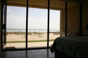 Ein Zimmer mit einer großen Schiebeglastür, die zum Blick auf einen Strand führt.