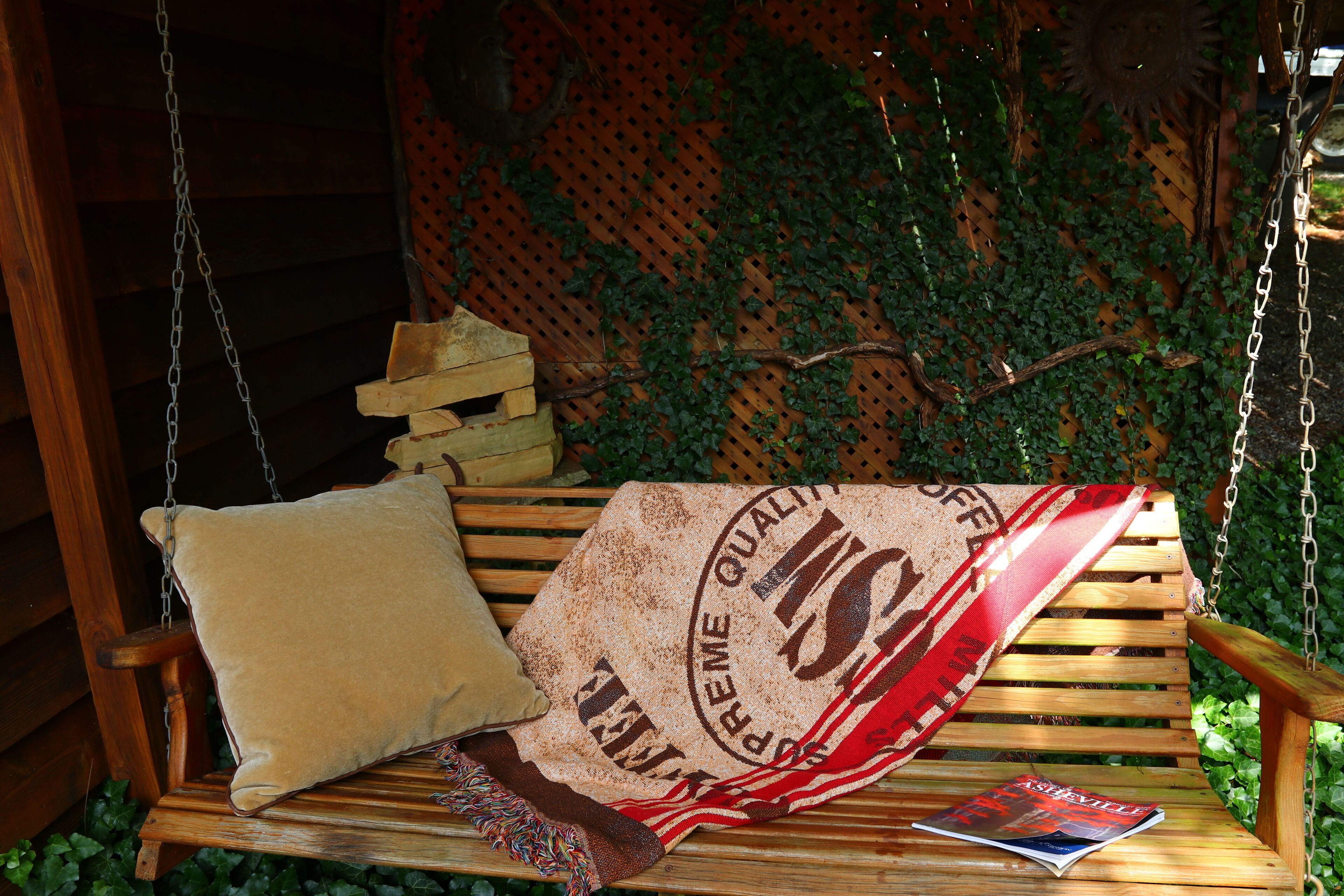 A wooden swing bench with a cushion and a magazine.