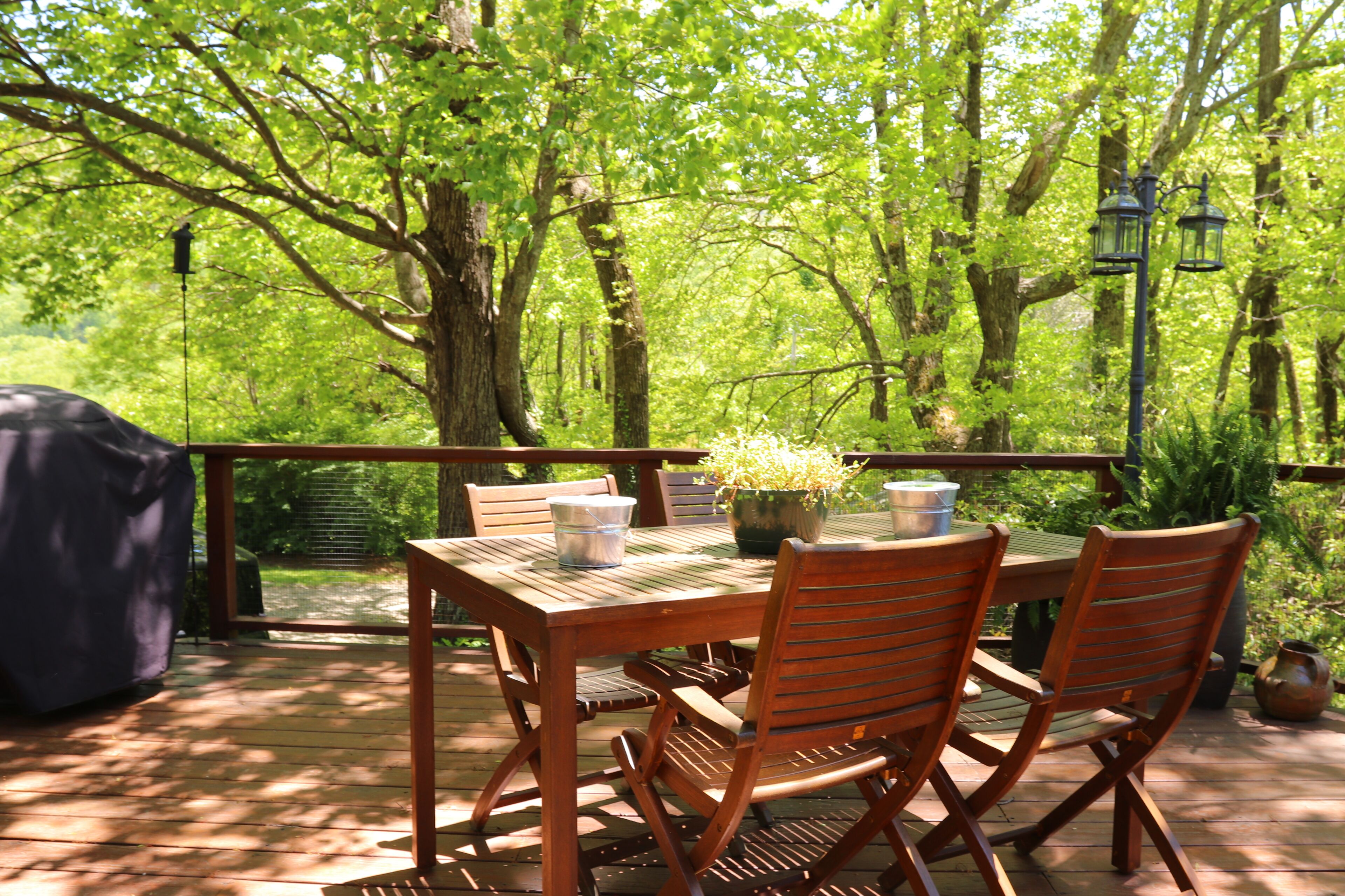 Une terrasse en bois à l’extérieur, avec une table et des chaises, entourée d’arbres.