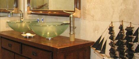 A bathroom with a wooden vanity, a glass sink, a large mirror, and a ship model.