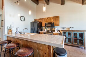 A kitchen with wooden cabinets, a large island with stools, a microwave, and a clock on the wall. - Spacious 3-Bedroom + Loft Condo at The Phoenix – Steps from the Slopes! (Steamboat Springs)