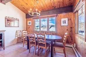 Un coin repas en bois, agrémenté d’un lustre, de grandes fenêtres et offrant une vue sur les montagnes.