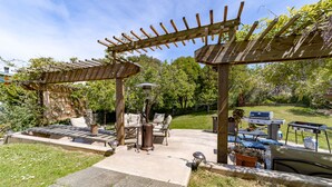 Een houten pergola met een terras, buitenmeubilair en een barbecue.