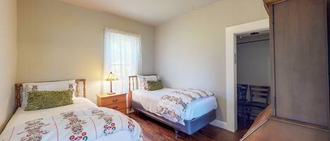 Quarto com duas camas, uma mesa de cabeceira, uma luminária e um guarda-roupa de madeira.