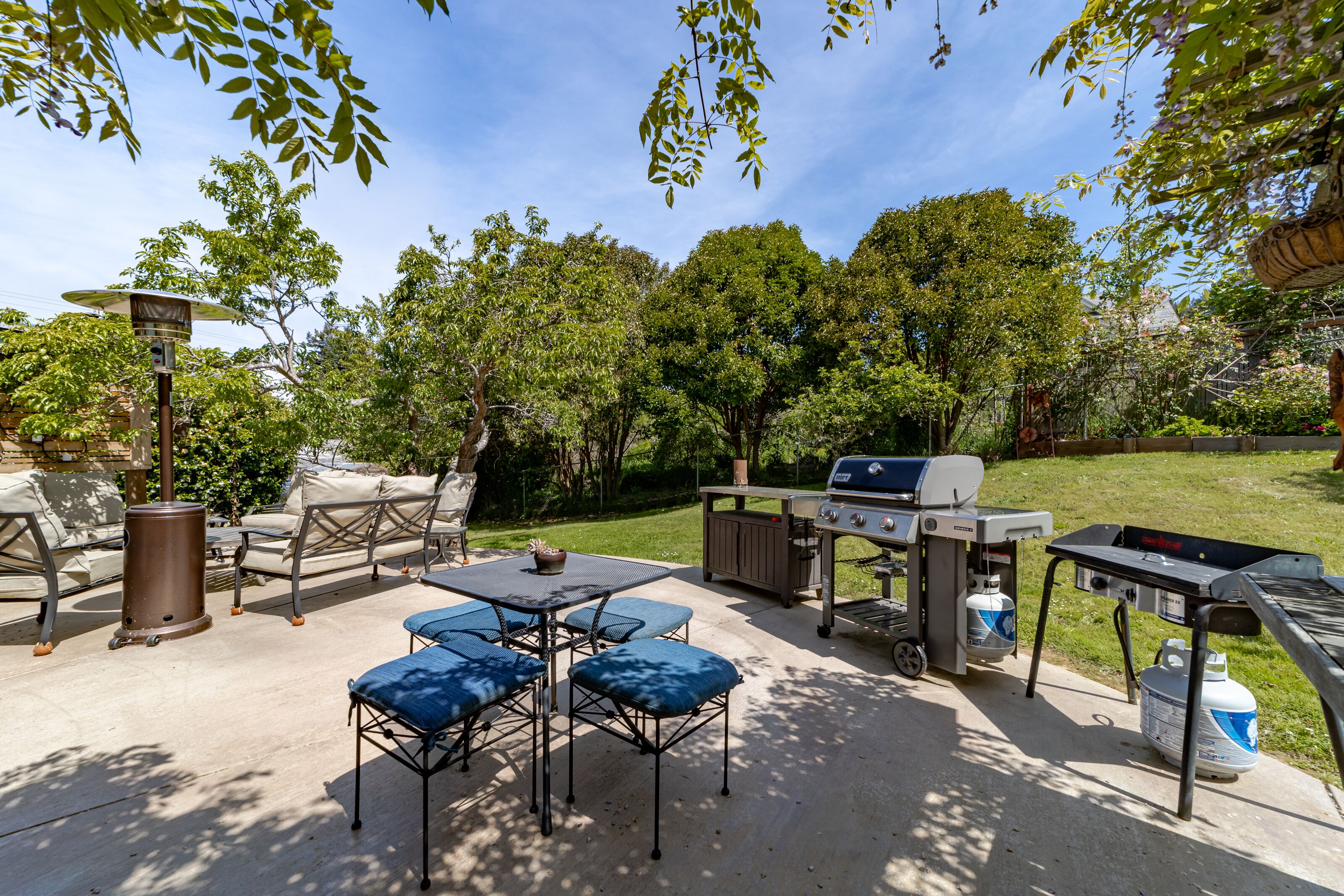 An outdoor patio with a grill, seating area, and a trash can.