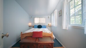 Une chambre à coucher avec un lit en bois, une table de chevet, un oreiller rouge et une fenêtre avec des rideaux.