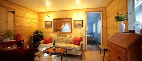 A cozy wooden cabin interior with a sofa, a coffee table, a dresser, and a mirror.