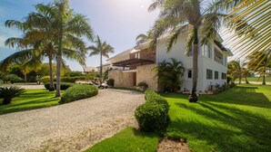 A modern house with a paved driveway, surrounded by well-maintained lawns and palm trees.
