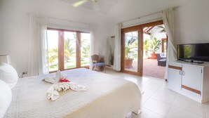 A hotel room with a large bed, a television, and a balcony with a view of palm trees.